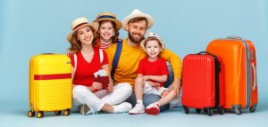 Family of four in bright red shirts sits on the floor with colorful luggage, ready for vacation against a blue backdrop.
