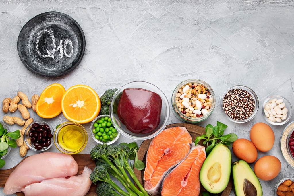 Alimente variate, printre care ficat, somon, pui, ouă, broccoli și avocado, lângă o placă cu inscripția Q10
